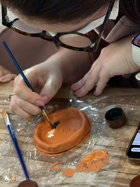 Participante pinta uma flor branca em uma peça laranja.