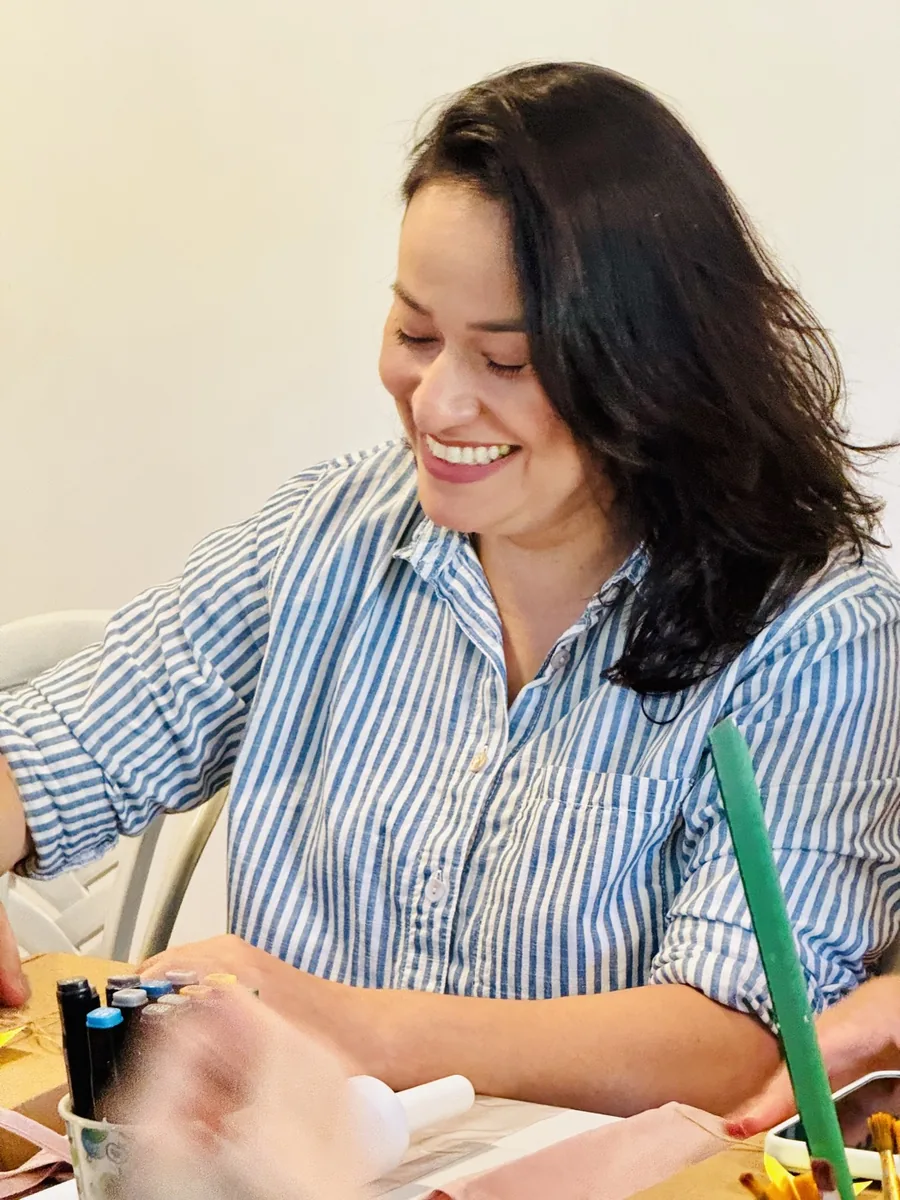 Participante sorri enquanto trabalha sua peça na mesa da oficina.