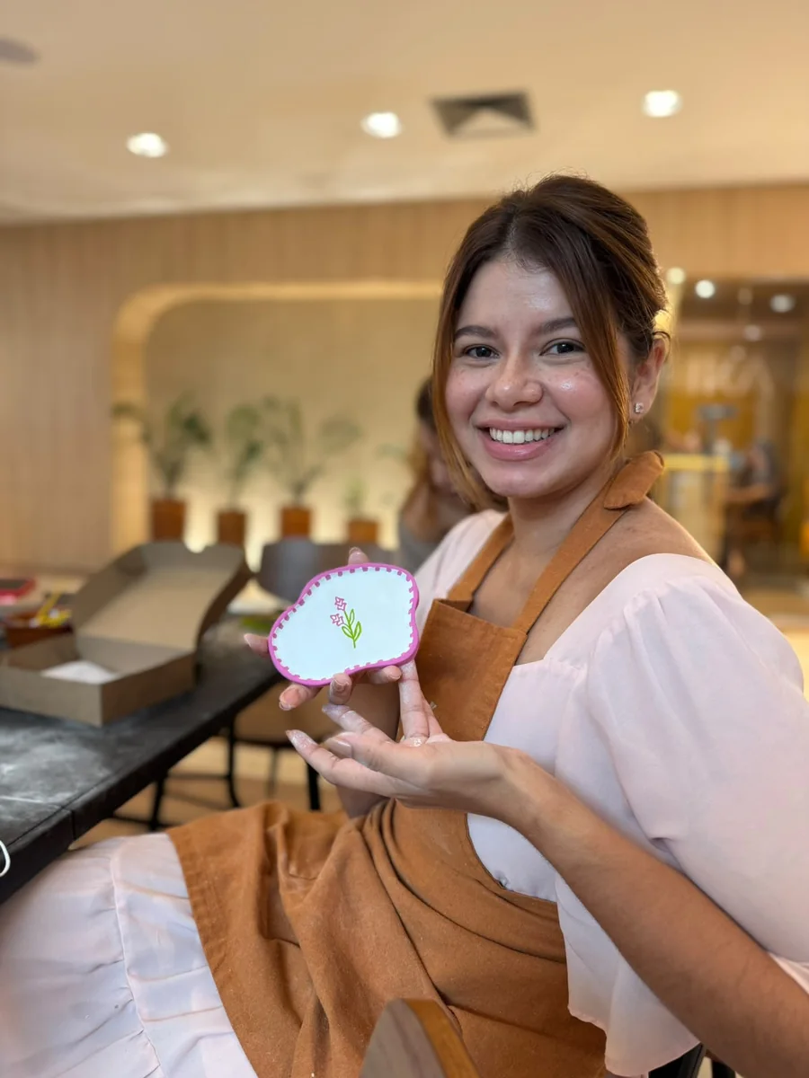 Participante sorri mostrando uma peça branca com borda rosa e desenho de flores.