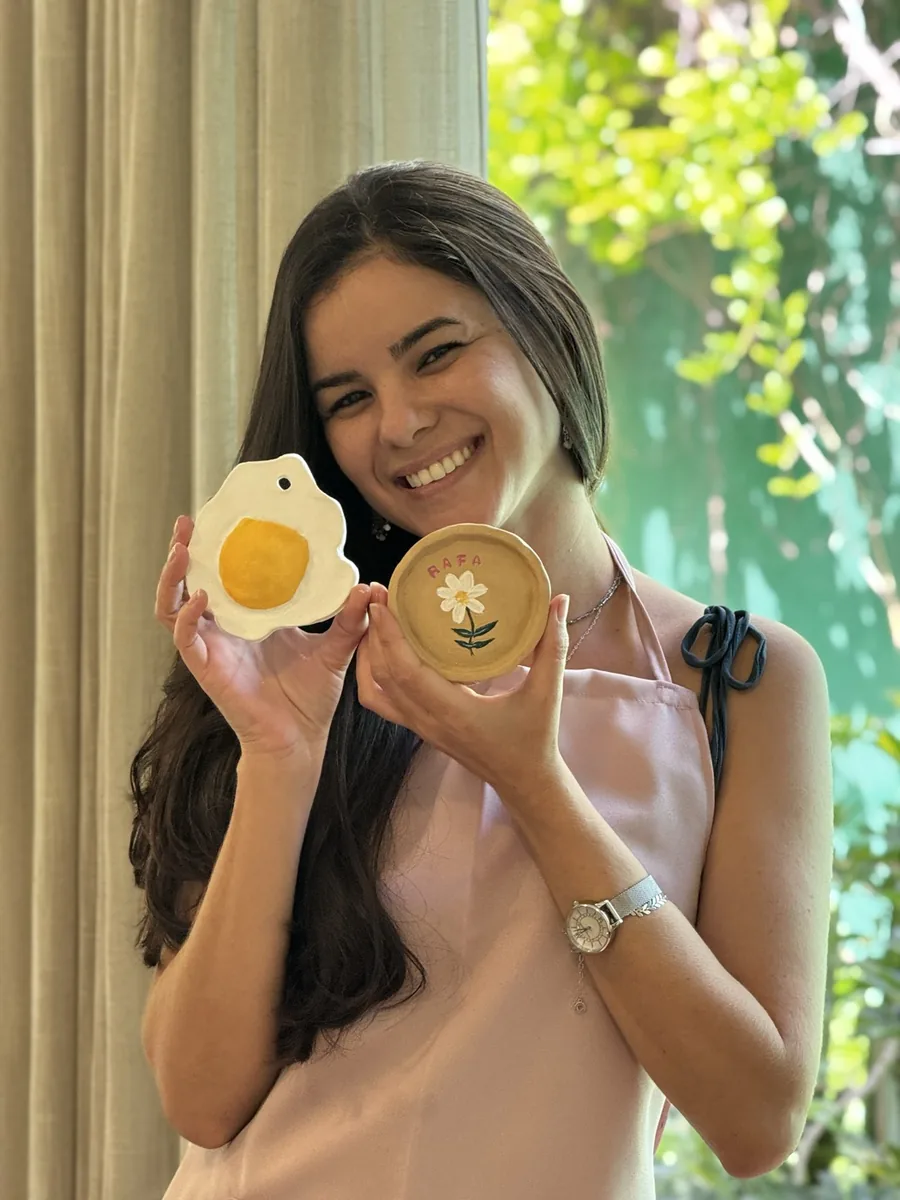 Participante sorri e mostra duas peças prontas, uma com flor e outra em formato de ovo.