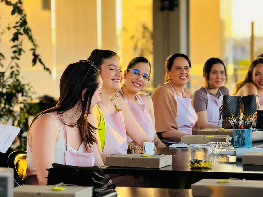 Participantes de avental rosa sorriem juntas à mesa de uma oficina no Na’vi.