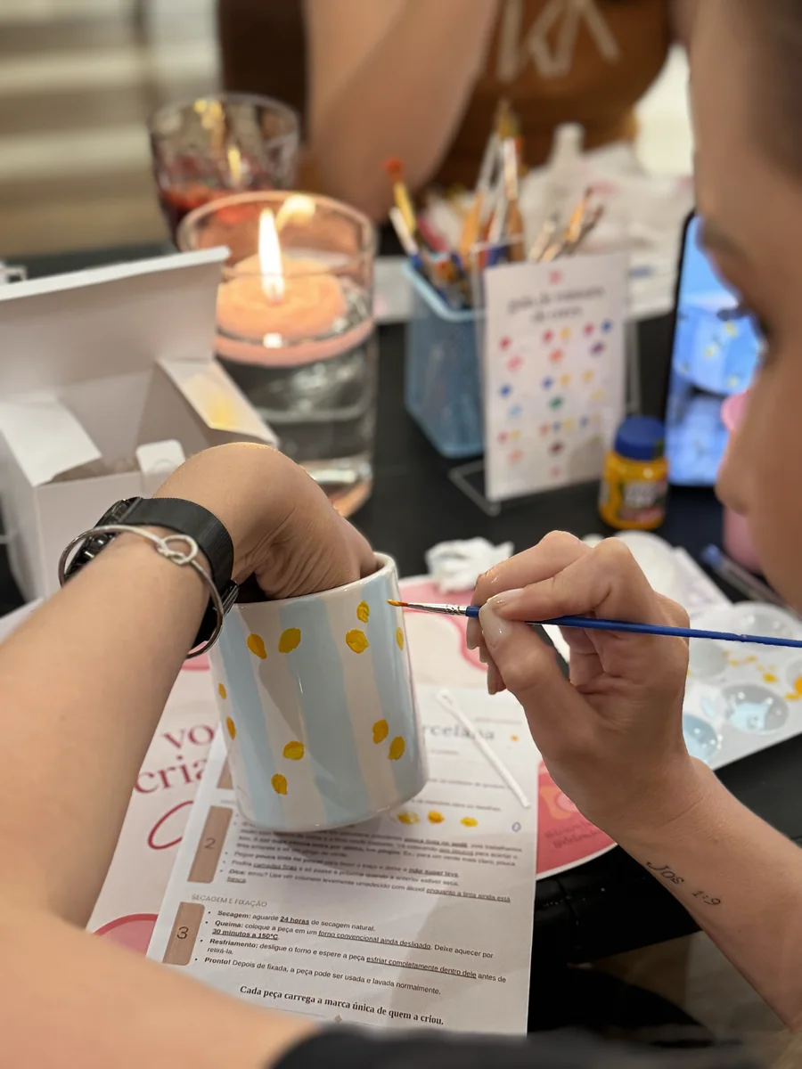 Participante pinta pequenos detalhes coloridos em uma caneca.