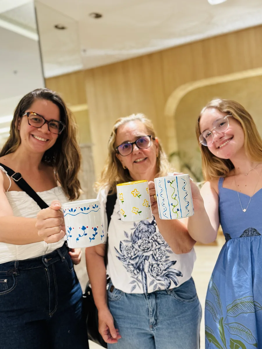 Três participantes mostram suas canecas pintadas durante um encontro.